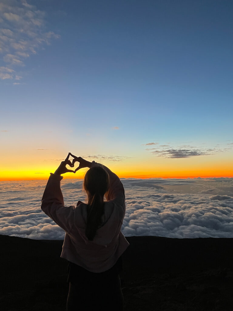 iPhone travel photo of woman silhouette in front of sunset above the clouds on Haleakala Volcano in Maui Hawaii